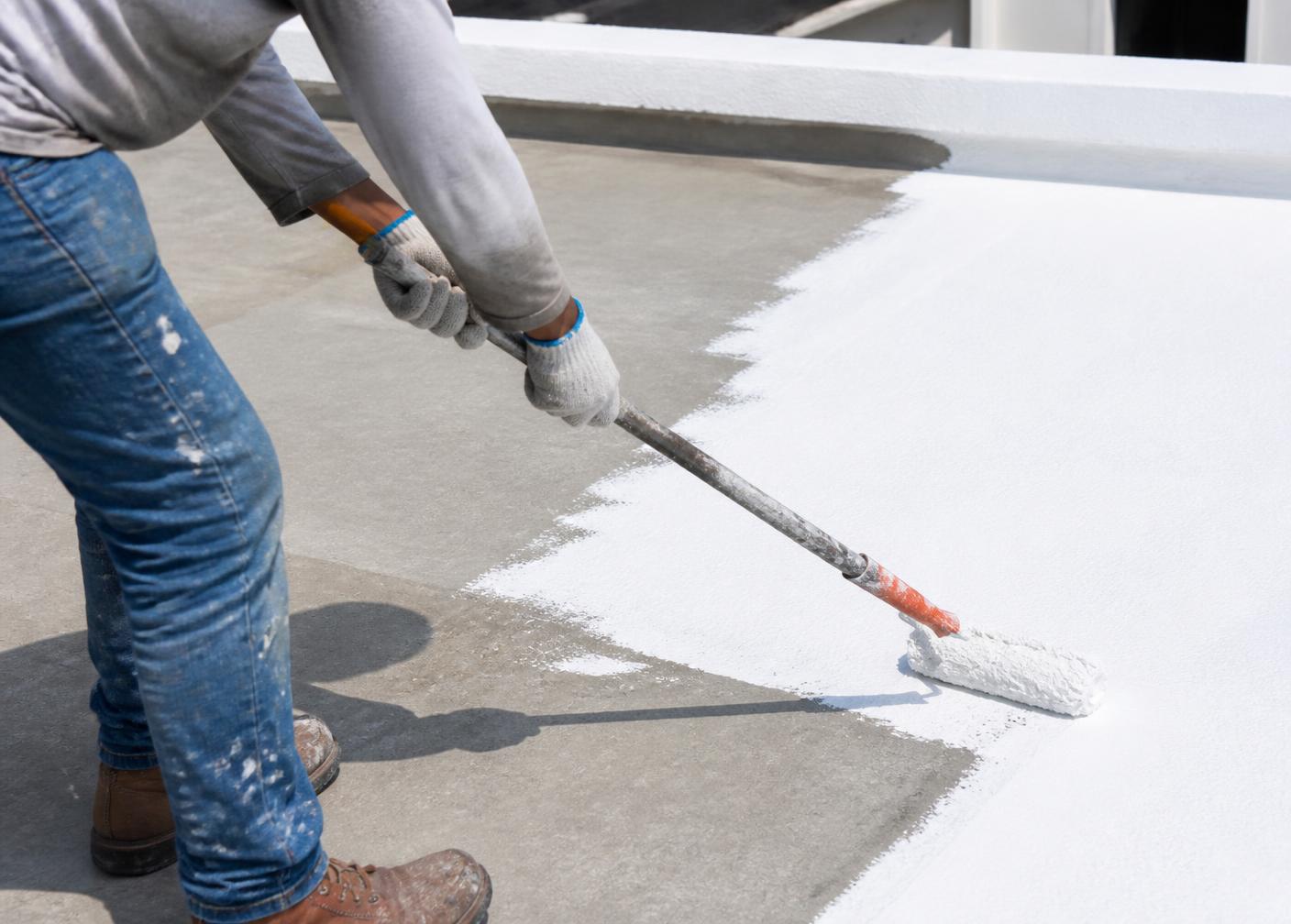 Operario aplicando con rodillo el recubrimiento impermeable blanco sobre hormigón